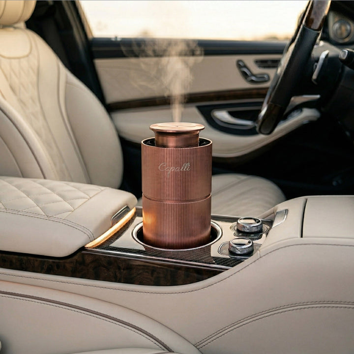 Rose gold Copalli Mini Diffuser with "Copalli" branding; placed in a luxury car cup holder, releasing a fine scent mist into a premium leather interior.