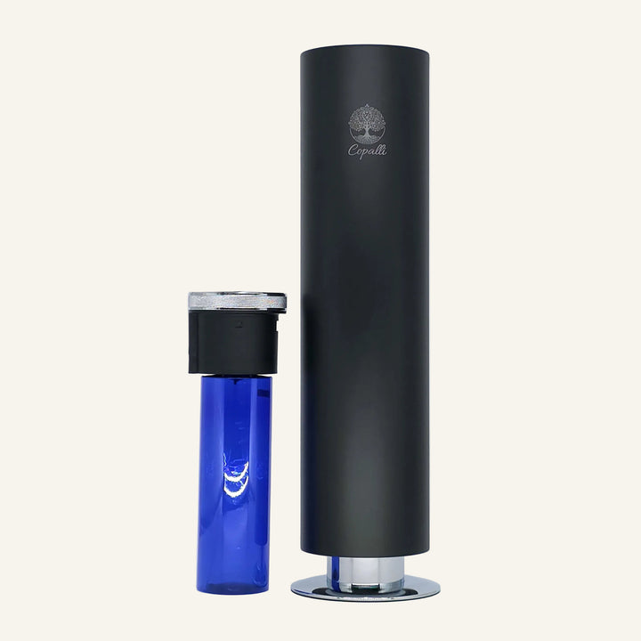 Our black Tower Pro Diffuser by Copalli, shown with its 1,000ml fragrance oil bottle removed to demonstrate the internal waterless diffusion system, set against a light cream background