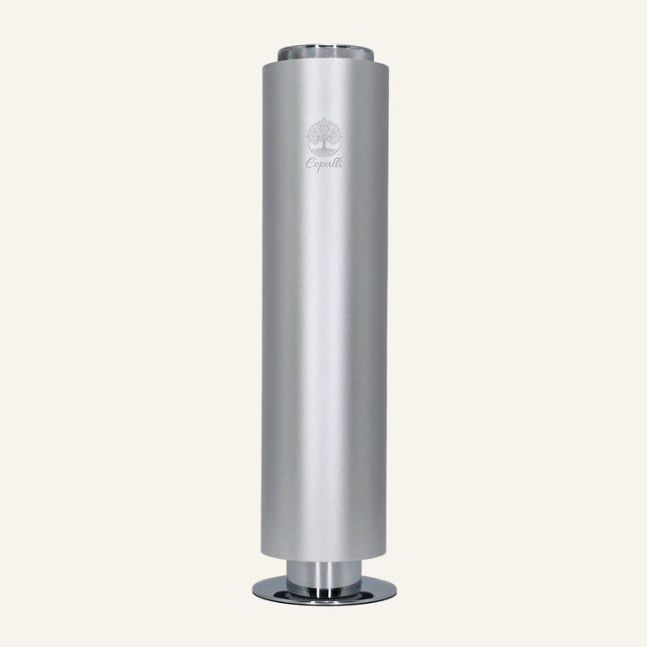 Our silver Tower Pro Diffuser by Copalli, featuring a sleek cylindrical aluminum body and minimalist tree logo, centered on a light cream background.